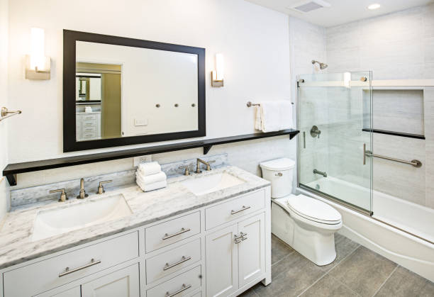 To the left of the picture is a white bathroom vanity with two sinks and a white marble countertop. There is also a toilet next to a shower-tub with rolling glass doors.