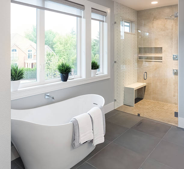 A beautiful white bathtub sits next to three large windows.